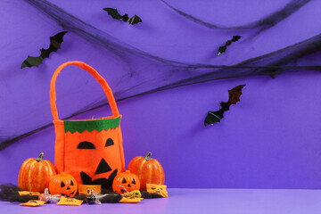 Halloween trick or treat concept with jack-o-lantern bucket candy and bats on purple background © itchaznong