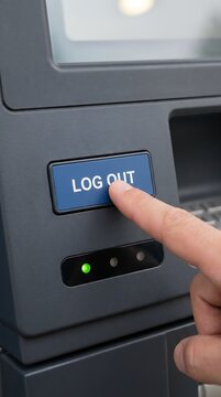 Close up of a person's finger pressing the blue log out button on a dark grey electronic terminal or atm machine in a public setting