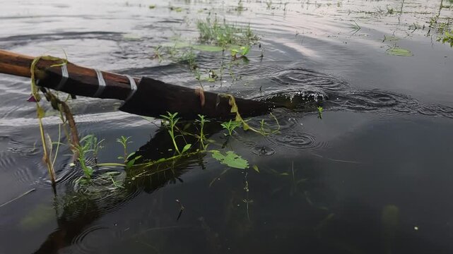A wooden oar stirring the dark water of a calm lake with gentle ripples