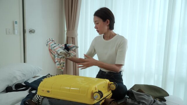 Stressed young woman struggling to pack an overfilled suitcase before a trip at home. Travel preparation luggage organization, packing stress. Vacation planning and travel anxiety concept.
