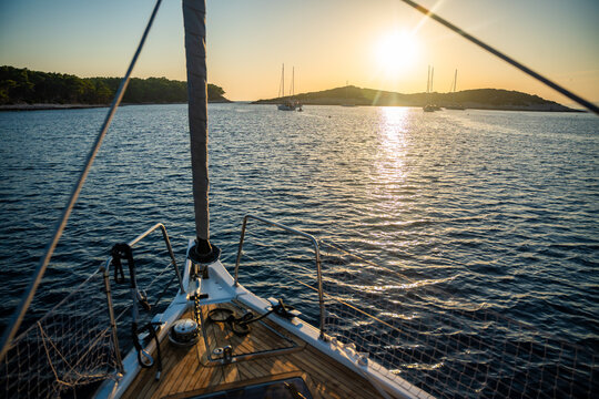 View from bow of sailing yacht anchored in quiet bay during golden sunset with other boats in distance. Concept of slow travel, sailing adventure, anchoring, freedom and peaceful evenings on water