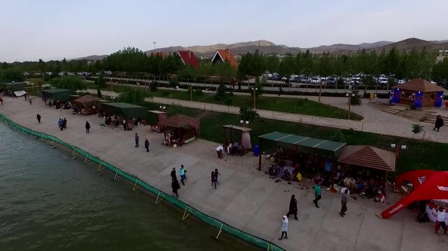 Detailed drone perspective of flyboard show with spectators gathered along the lake promenade and colorful tents visible.