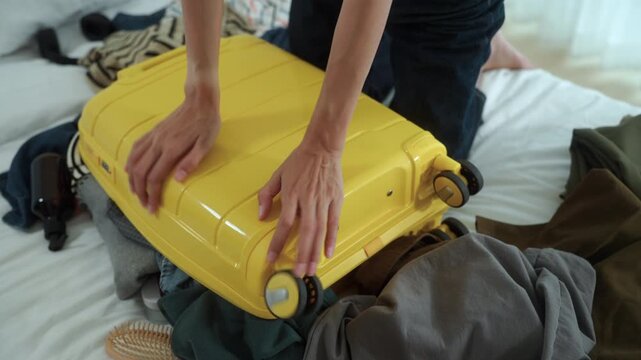 Close-up Stressed young woman struggling to pack an overfilled suitcase before a trip at home. Travel preparation, luggage organization, packing stress. Vacation planning and travel anxiety.
