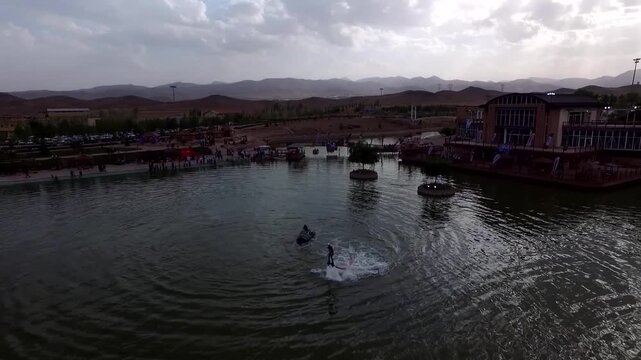 Professional aerial footage shows flyboard rider performing near shore with people and boats visible in recreational zone.