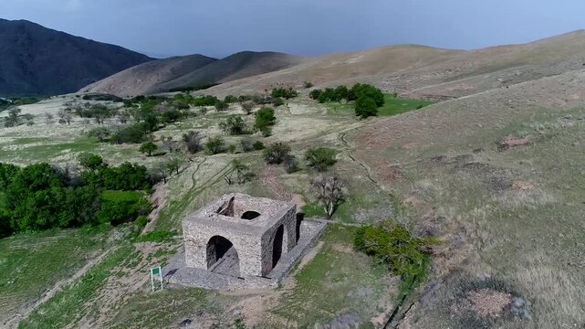 Scenic drone footage displays fire temple ruins on elevated position overlooking green valley and distant mountain ranges.