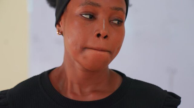 Close up black woman thoughtful expression, headband, looking down with soft gaze against whiteboard backdrop, quiet introspection, subdued lighting, natural skin texture, candid portrait conveying
