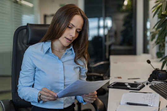 Confident stylish european woman sitting at workplace, executive leader manager reading documents.