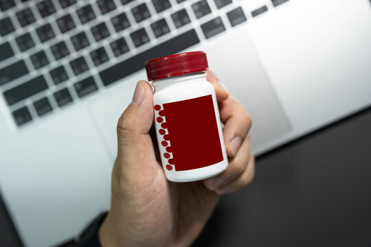 hand holding medicine pill bottle over laptop workspace table concept of workaholic health supplement. office syndrome, stress management, workaholic lifestyle, brain and energy supplements, health 