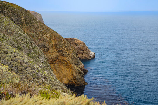 Rugged coastal cliffs draped in green scrub descending to dark blue Pacific water under a hazy horizon on Santa Cruz Island, Channel Islands National Park, California
