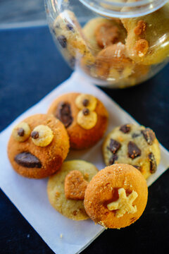 Close-up shot of creative handmade cookies with fun monster face, star, and heart toppings served on white baking paper next to a clear plastic cookie jar. Ideal for concepts of home baking, kids part