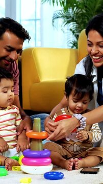 Indian Asian young parents playing with twin infant babies using colorful ring stacking toy at home, guiding fine motor learning activity and clapping with joy after completing playful task together