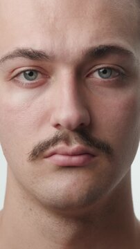 Frontal studio close-up portrait of a young shirtless Caucasian man with a mustache looking directly at the camera with a neutral serious expression against a clean bright white background.