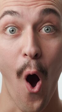 Frontal studio close-up portrait of a young Caucasian man with a mustache looking at camera with a surprised open-mouth expression on a white background.