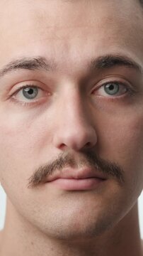 Frontal studio POV portrait of a young Caucasian man with a mustache talking and nodding during an online video call against a bright white background.