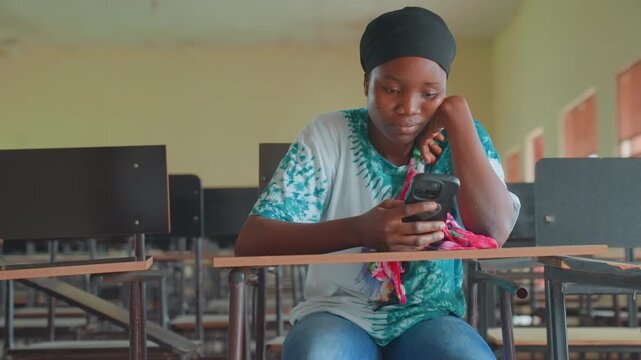 Black mother checking phone in classroom, empty desks and computer monitors, soft sunlight through windows, headscarf and denim, scrolling messages, quiet reflective mood, anticipation and resilience