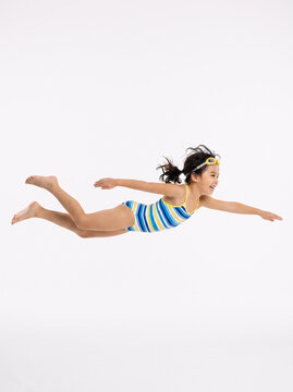 Editorial shot of a child pretending to swim in air, horizontal pose, white background, creative illusion