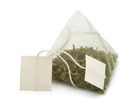 Pyramid tea bag filled with green tea leaves and a paper tag isolated on white background with copy space