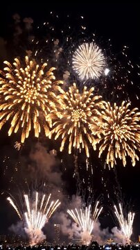 Golden Fireworks Display in Night Sky Over City Skyline - A spectacular multi-colored fireworks display illuminates the dark night sky, casting a golden glow over a distant city skyline.
