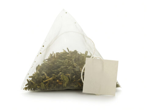 Pyramid tea bag with green tea leaves and empty label isolated on white background with copy space