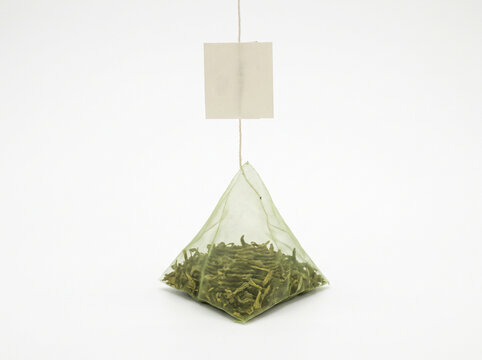 Pyramid green tea bag hanging with a paper tag isolated on a clean white background with copy space
