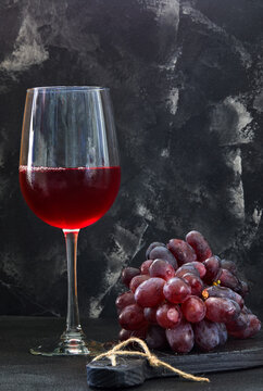 Glass of wine with grapes on a black wooden stand and dark background