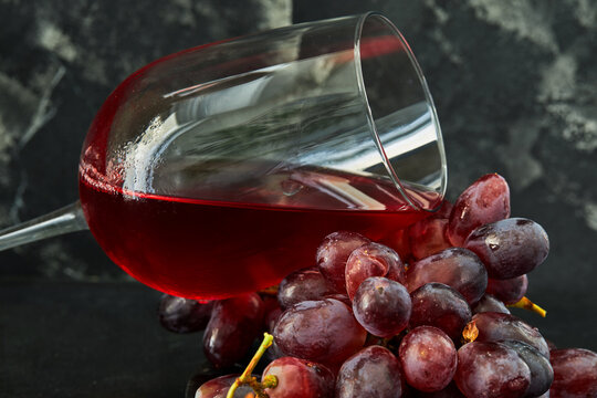 Glass of wine with grapes on a black wooden stand and dark background