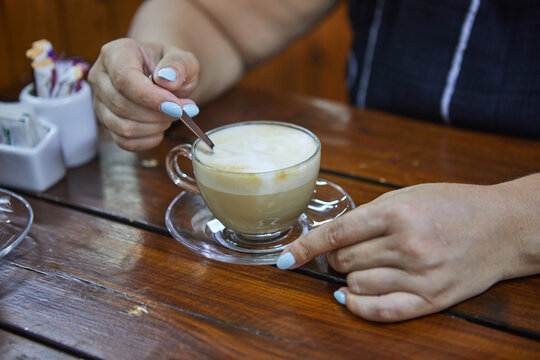 Close up of woman hands holding a cappuccino coffee cup. Female with coffee cup sitting at cafe.