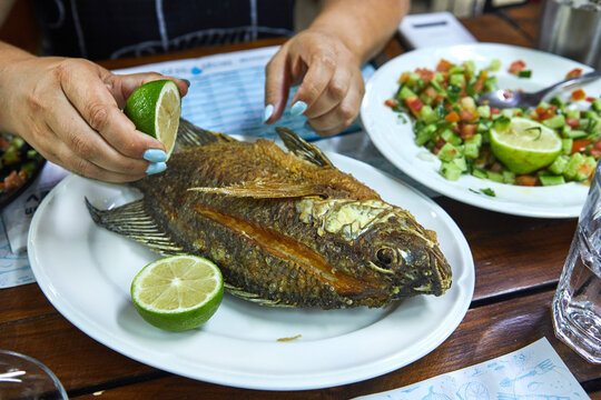 Hands of a woman holding a lemon and pouring fried fish on a plate. Slave restaurant.