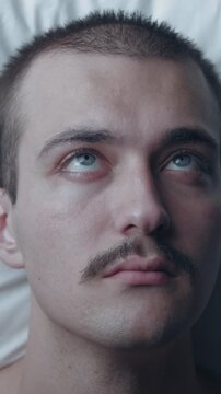 Top-down view portrait of a thoughtful young Caucasian man lying awake in bed on a white pillow, suffering from insomnia, worry, and deep thoughts.