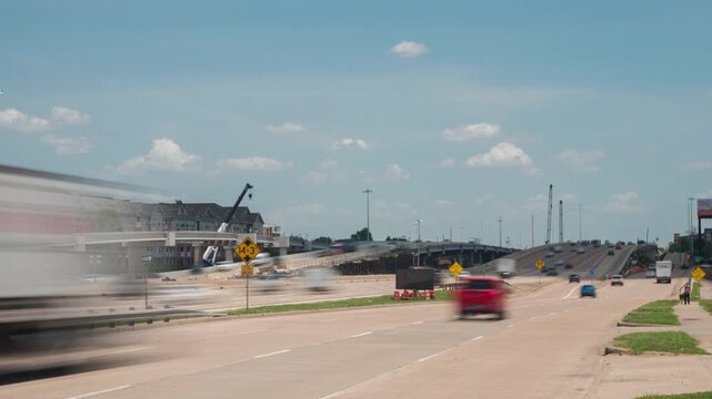 Aerial drone establishing shot of Caterpillar construction equipment operating alongside Interstate 10 West in Houston, Texas, with steady commuter traffic on the freeway.