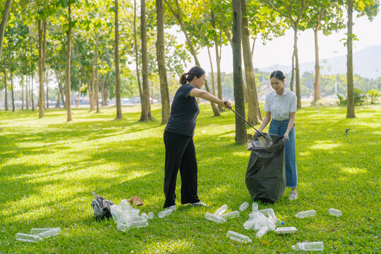 Asian Women Volunteers Collecting Plastic Bottle Garbage into Trash Bag in Green Park for Environmental Protection and Recycling Concept