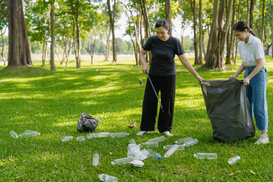 Asian Women Volunteers Collecting Plastic Bottle Garbage into Trash Bag in Green Park for Environmental Protection and Recycling Concept