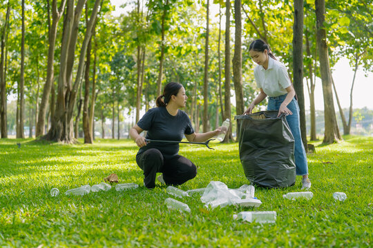 Asian Women Volunteers Collecting Plastic Bottle Garbage into Trash Bag in Green Park for Environmental Protection and Recycling Concept