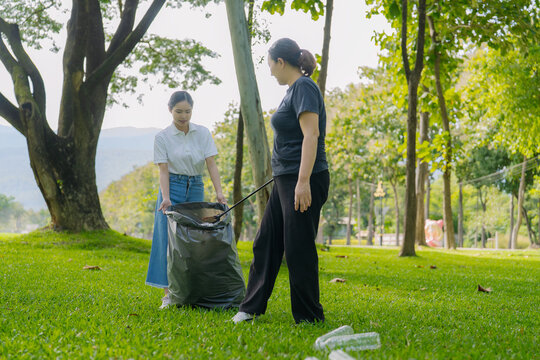 Asian Women Volunteers Collecting Plastic Bottle Garbage into Trash Bag in Green Park for Environmental Protection and Recycling Concept