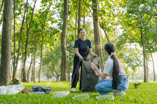 Asian Women Volunteers Collecting Plastic Bottle Garbage into Trash Bag in Green Park for Environmental Protection and Recycling Concept