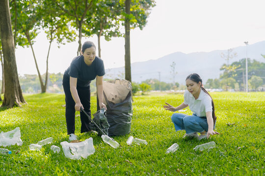 Asian Women Volunteers Collecting Plastic Bottle Garbage into Trash Bag in Green Park for Environmental Protection and Recycling Concept