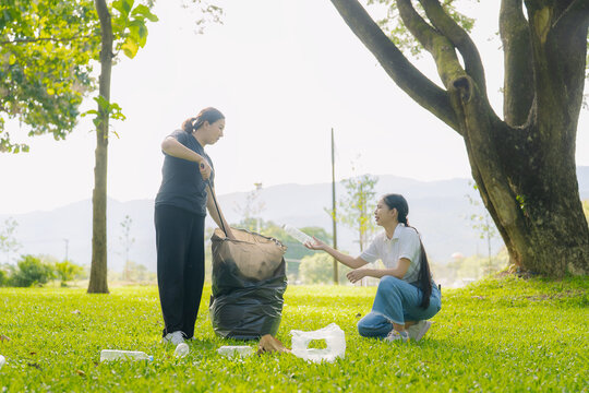 Asian Women Volunteers Collecting Plastic Bottle Garbage into Trash Bag in Green Park for Environmental Protection and Recycling Concept