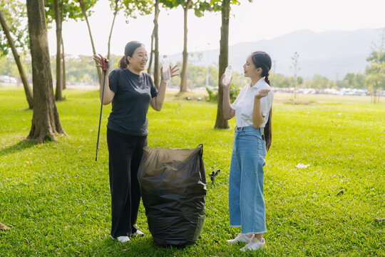 Asian Women Volunteers Collecting Plastic Bottle Garbage into Trash Bag in Green Park for Environmental Protection and Recycling Concept