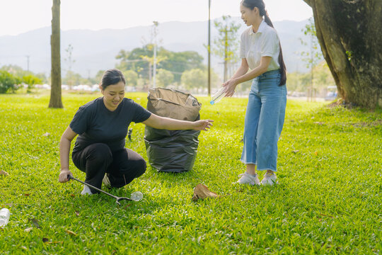 Asian Women Volunteers Collecting Plastic Bottle Garbage into Trash Bag in Green Park for Environmental Protection and Recycling Concept