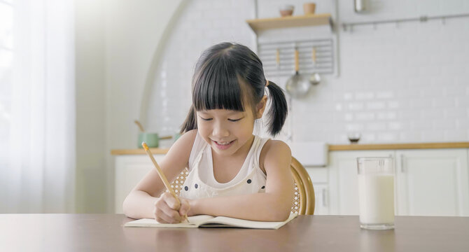 Portrait of Asian girl writing in a book in elementary school. Student girl study home work primary Children with pencil or pen at home. Education knowledge back to school concept