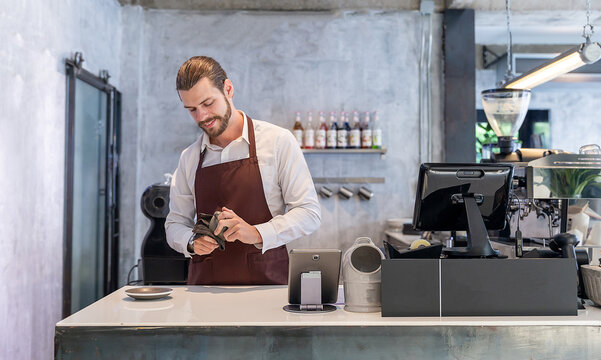 Startup successful sme small business entrepreneur owner man cleaning cup at counter bar coffee shop restaurant. Portrait of young caucasian seller man successful barista cafe owner job modern worker.