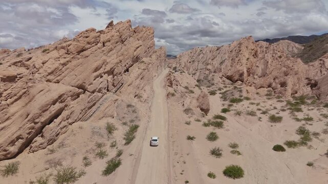 Car driving between towering rocks in Quebrada de las Flechas, aerial symmetrical rearview follow