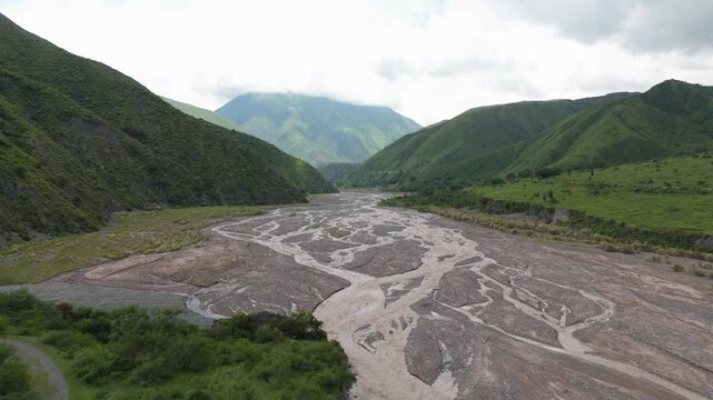 Braided river valley floodplains framed by lush mountains near Puente Chorro Blanco, aerial establishing forward downstream