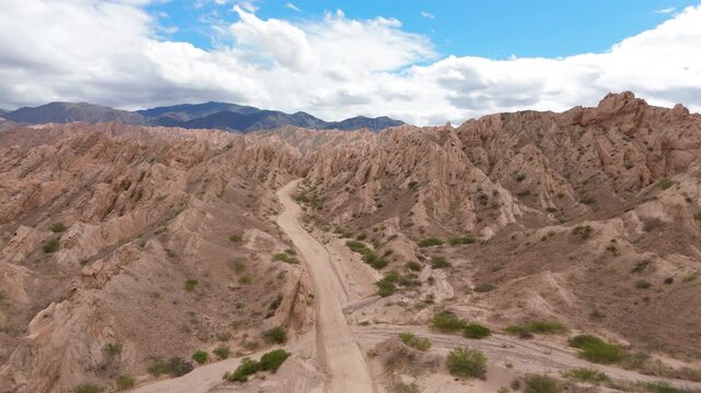 Car driving along dirt road in Quebrada de las Flechas sandstone landscape, aerial dolly forward to jagged geologic structure