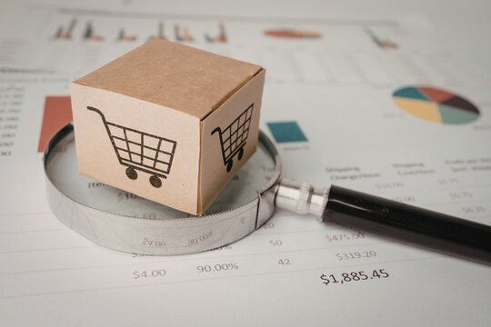 Magnifying glass resting on a cardboard delivery box with shopping cart icon e commerce magnifying shopping