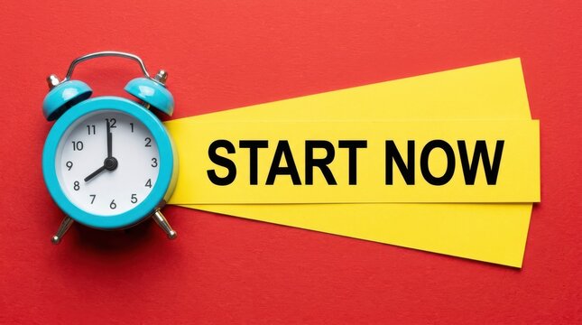 Retro blue alarm clock next to yellow paper sign with text start now isolated on solid red colored wall background.