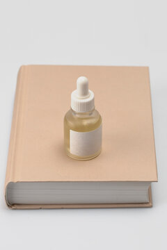 Minimalist skincare aesthetic featuring a glass dropper bottle with golden serum placed on a neutral beige book. Clean studio lighting highlights the elegant simplicity of a modern beauty routine.