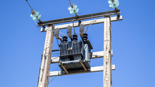 Transformador el&eacute;ctrico en poste de madera bajo cielo azul