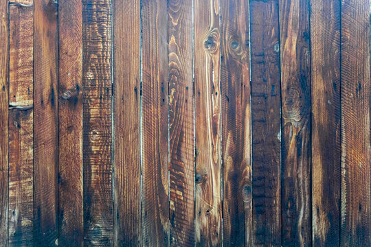A weathered, dark brown fence made of vertical wooden planks with a small gap between them. The wood grain and nail attachment points are visible.