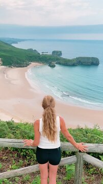 woman standing at viewpoint looking at beach and ocean landscape in asturias spain